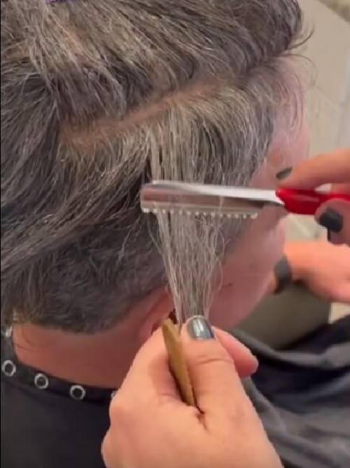 a stylist cuts a man's CNC hair replacement system to blend seamlessly with his bio hair